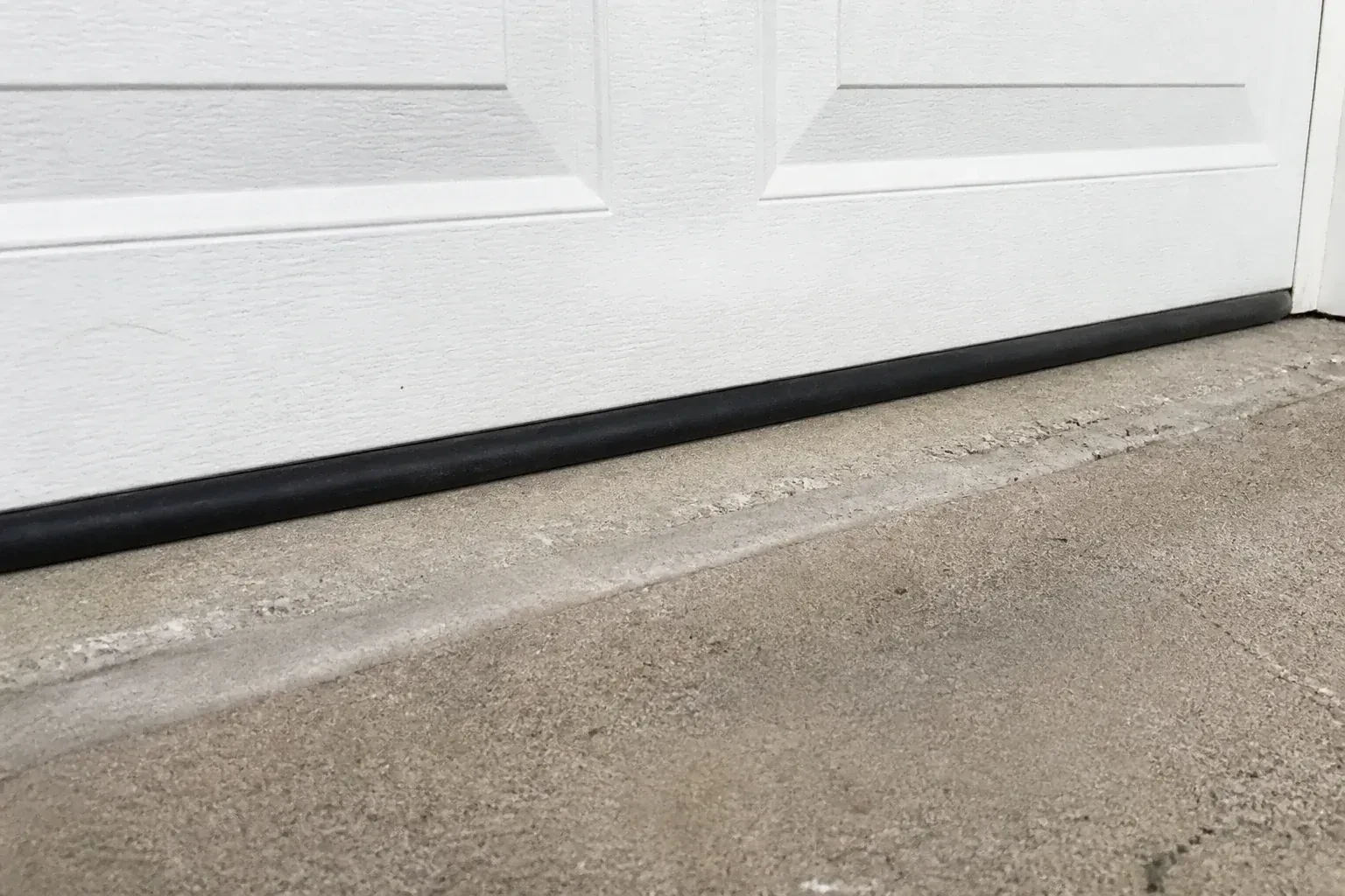 Black bottom seal along a closed white garage door at a concrete threshold. — Garage Door Bottom Seal Replacement, Cramahe