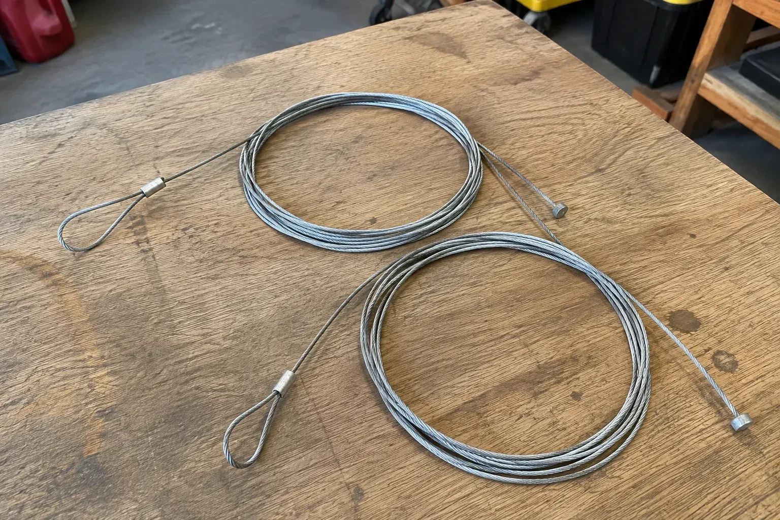 Two coiled steel cables with loop and stop ends on a workbench. — Garage Door Cable Replacement, Cobourg